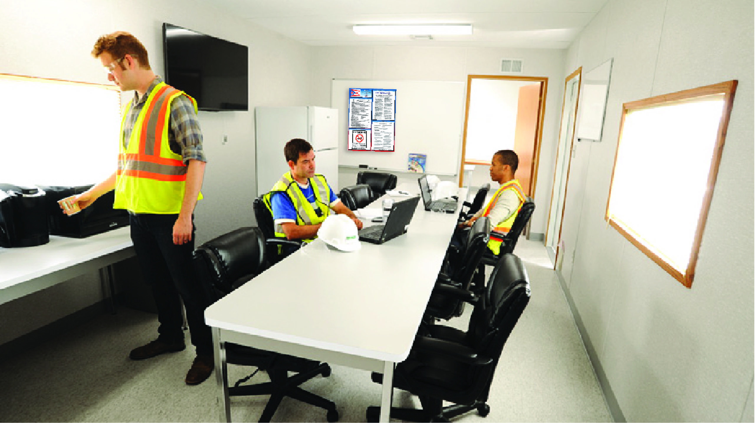 Three construction workers, wearing safety vests and sitting in an office with labor law poster on the wall